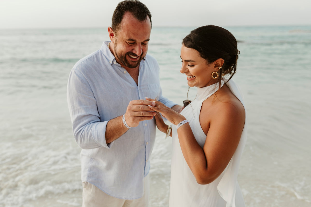 A man places a ring on a woman's finger as they laugh on the beach
