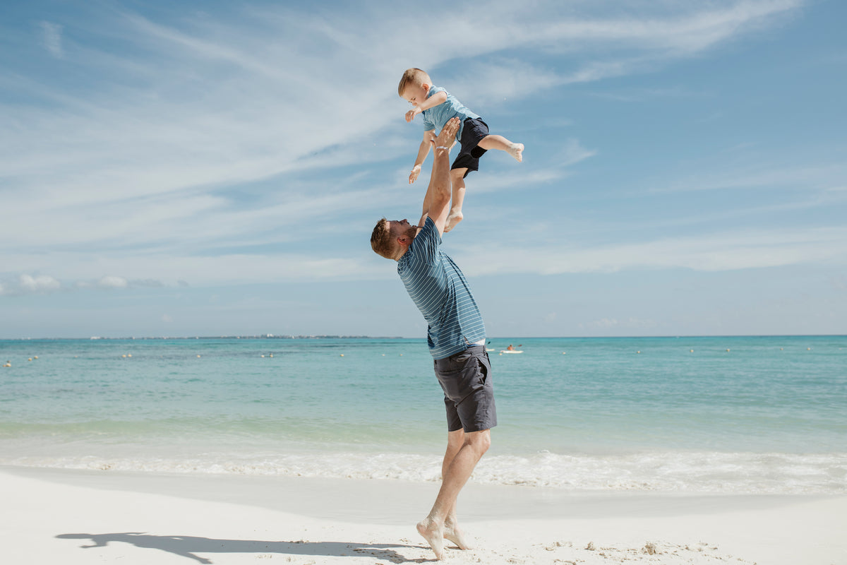 A man on a white sand beach at Grand Fiesta Americana Coral Beach Cancún lifts a toddler into the air