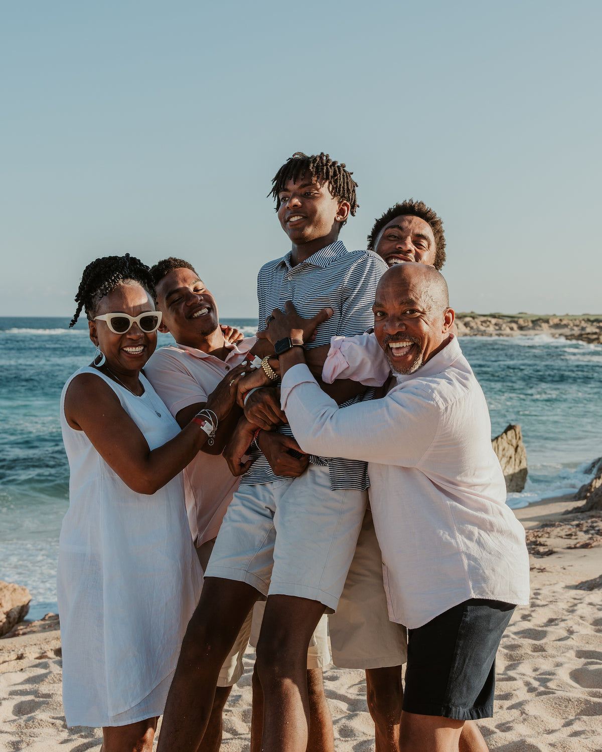 A family of five laughs together on a beach at Fiesta Americana Los Cabos with ocean waves behind them