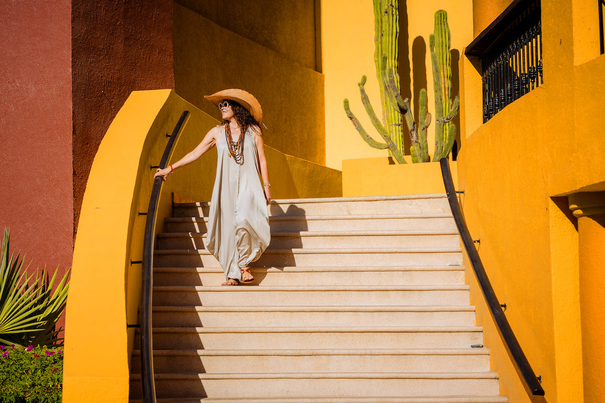A woman in a straw hat descends yellow stairs at Fiesta Americana Los Cabos, cactus behind her