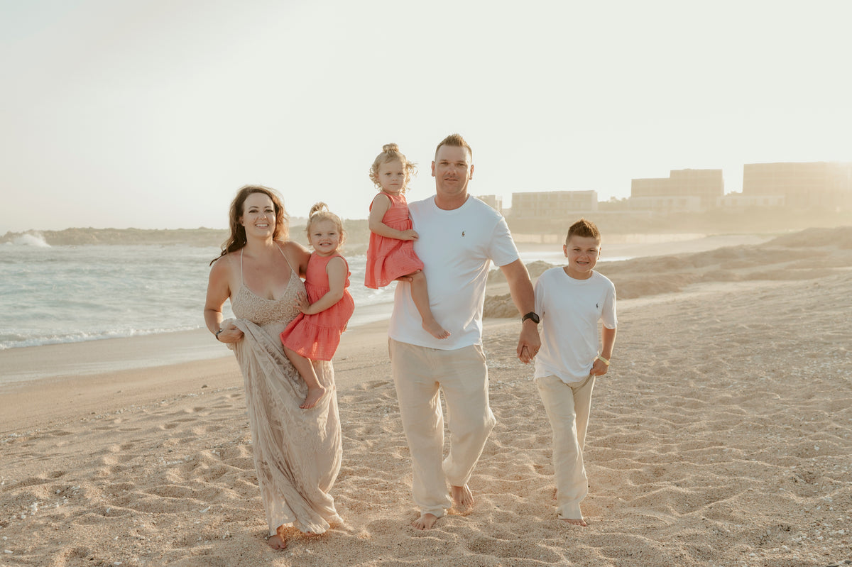 Family of five walking on the beach at Fiesta Americana Los Cabos, buildings visible in the hazy background