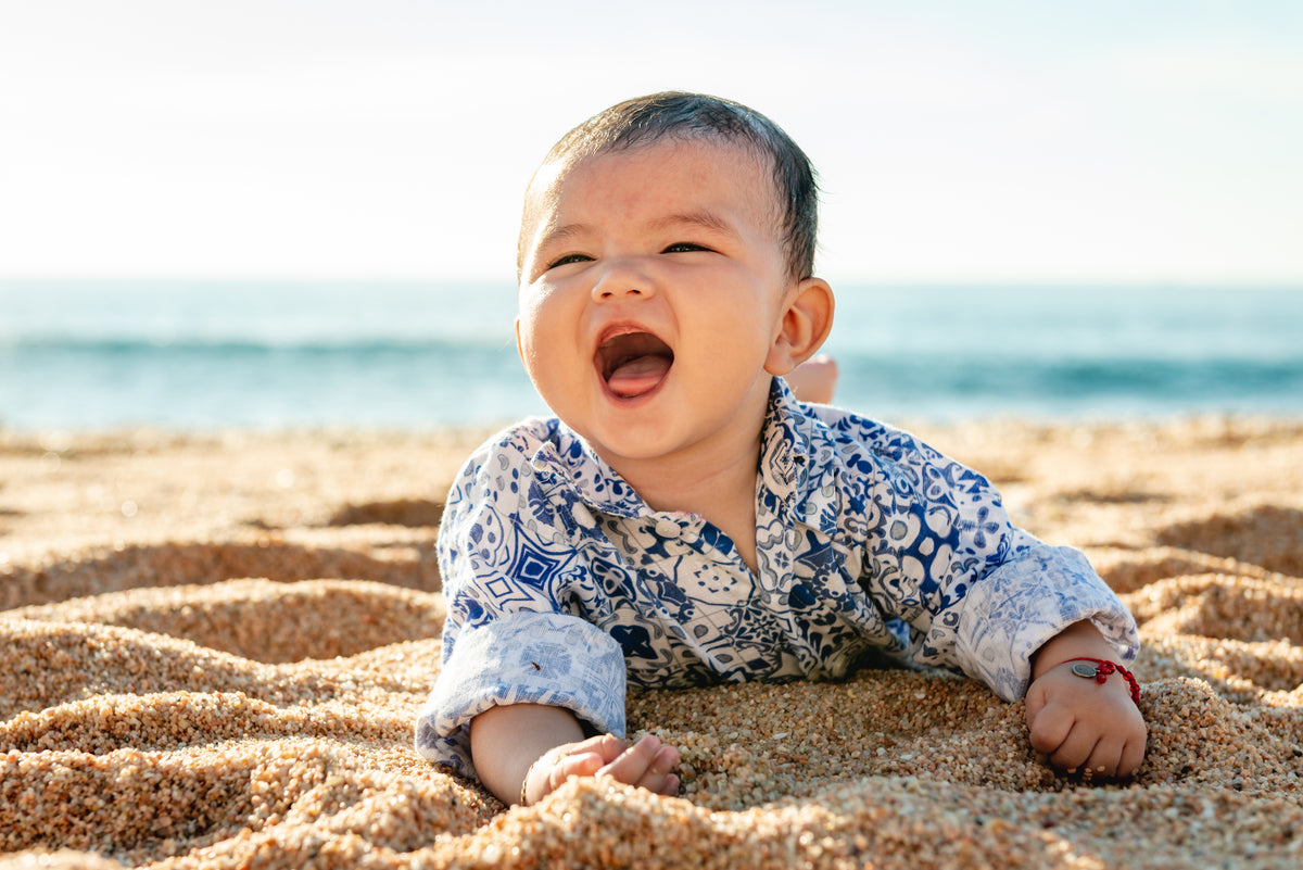 Baby laughing while lying on the sand at Fiesta Americana Los Cabos, ocean in the background
