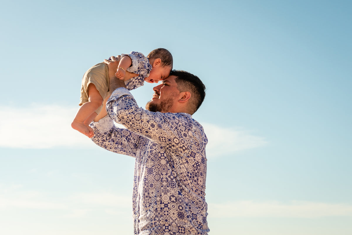 A man holds a baby overhead against a clear sky at Fiesta Americana Los Cabos