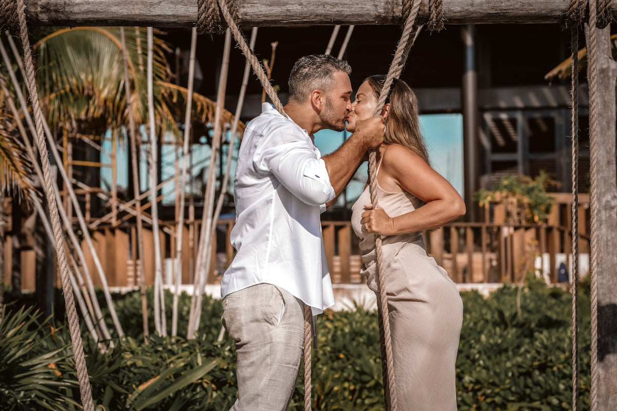 Couple kisses between rope swings at a beach club during a romantic vacation photoshoot
