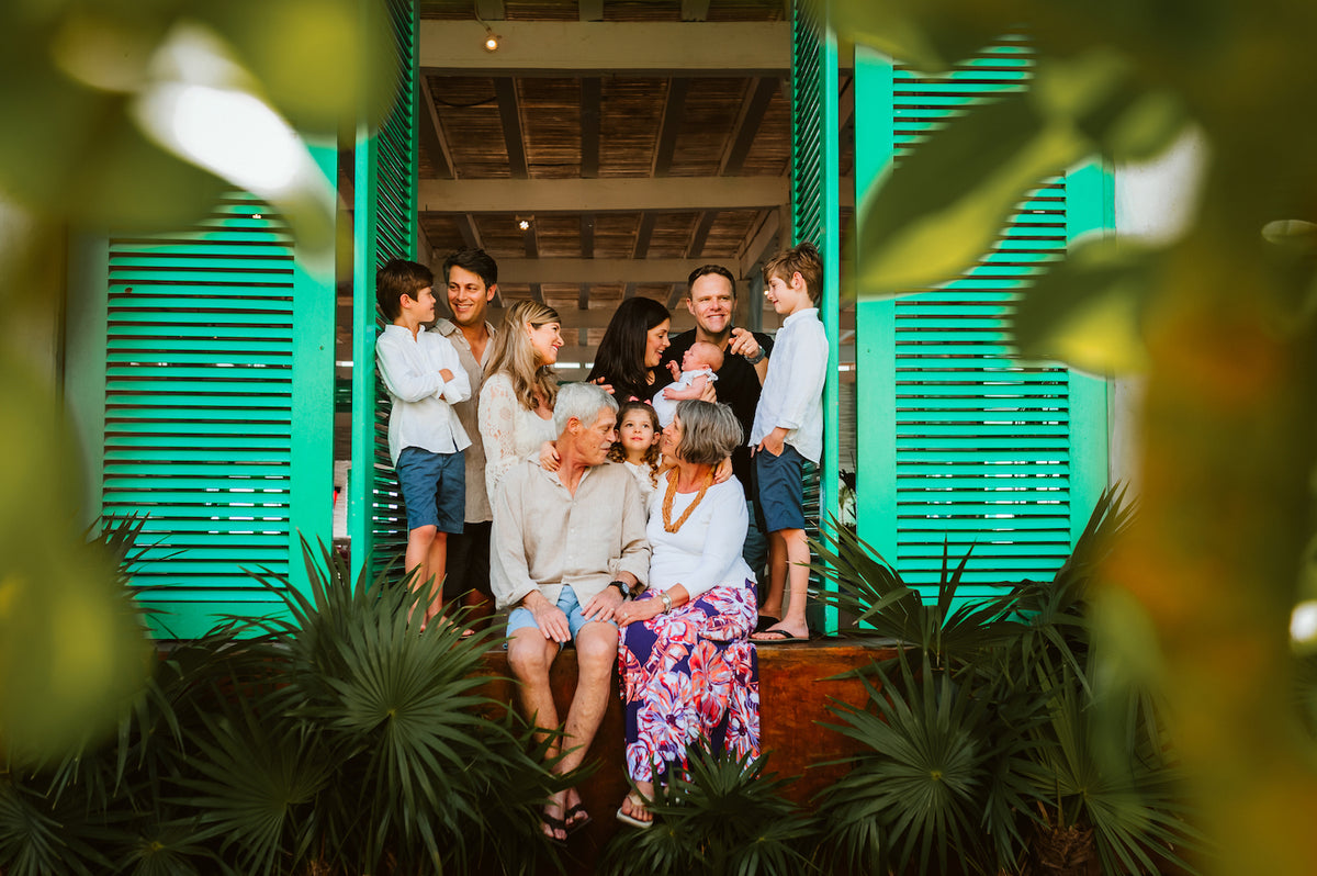 Multigenerational family gathered in a turquoise shuttered doorway framed by palm leaves
