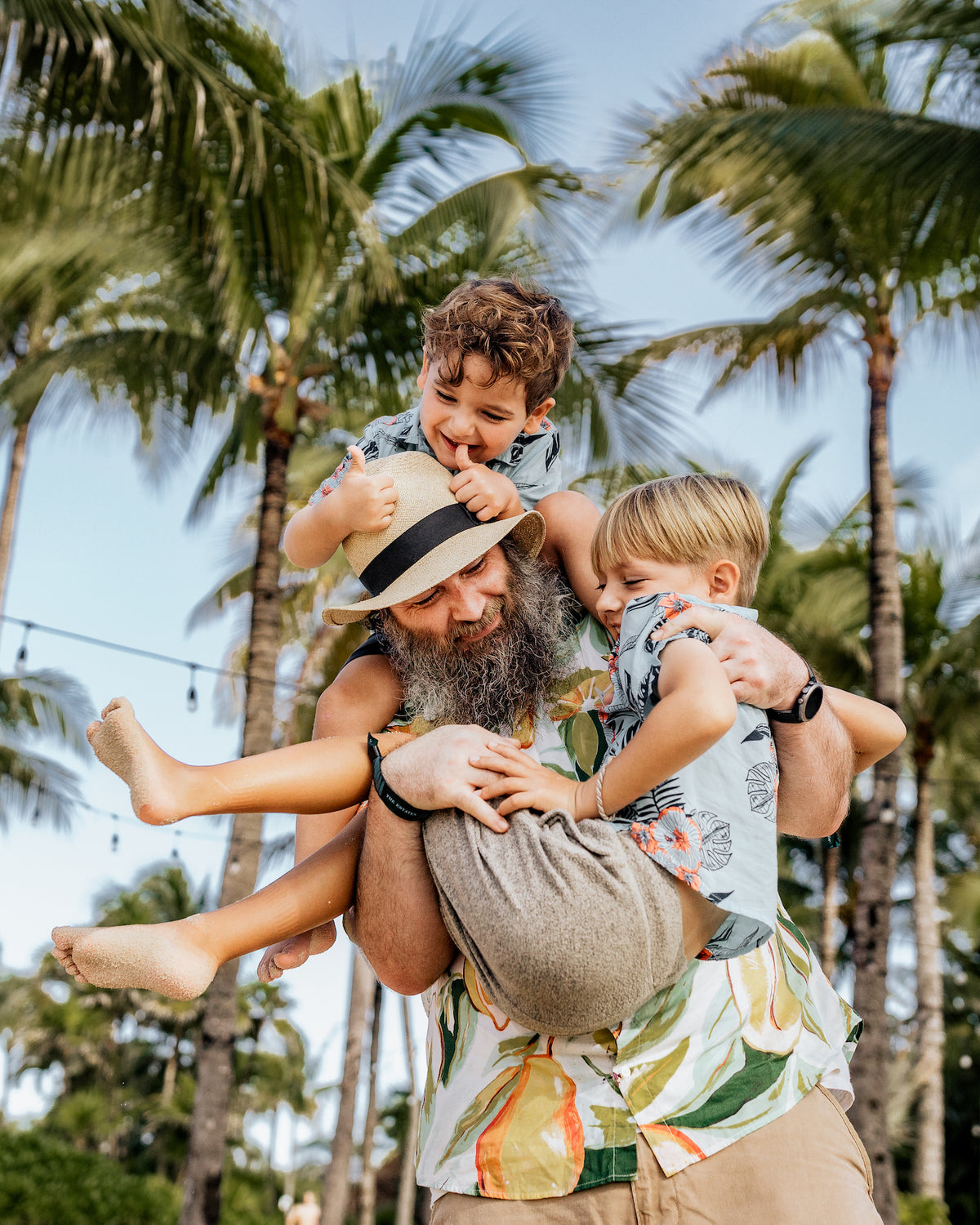 Bearded dad carries his two giggling boys on his shoulders under palm trees at Vidanta Riviera Maya
