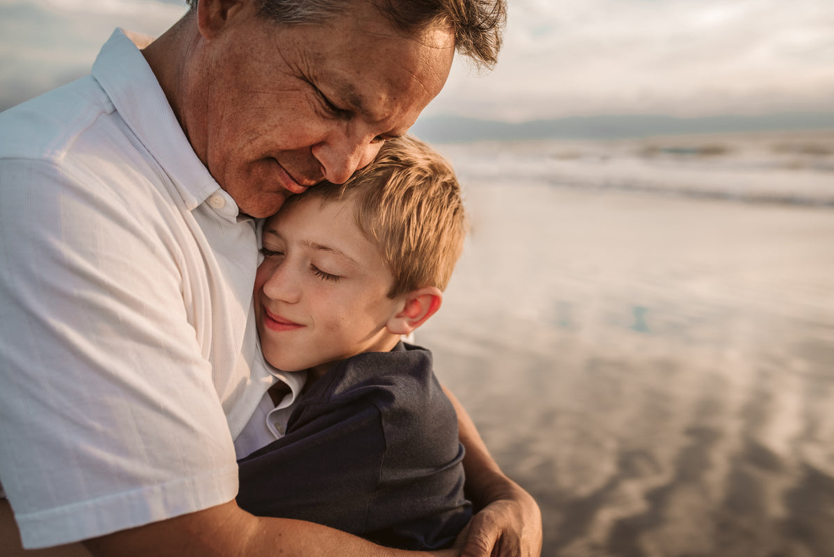 Grandfather hugs his grandson close on the wet sand at sunset during a family photoshoot