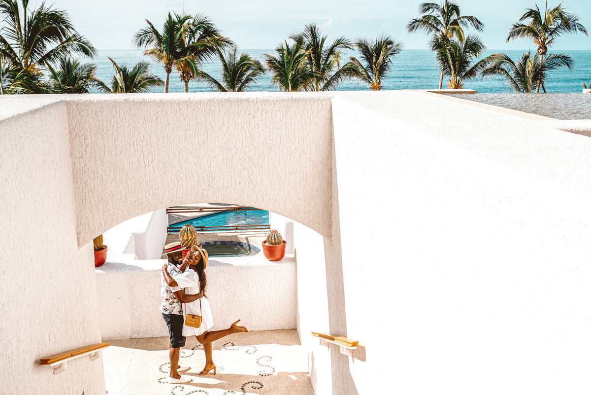 A couple embraces under a white archway at Marquis Los Cabos, with palm trees and ocean beyond