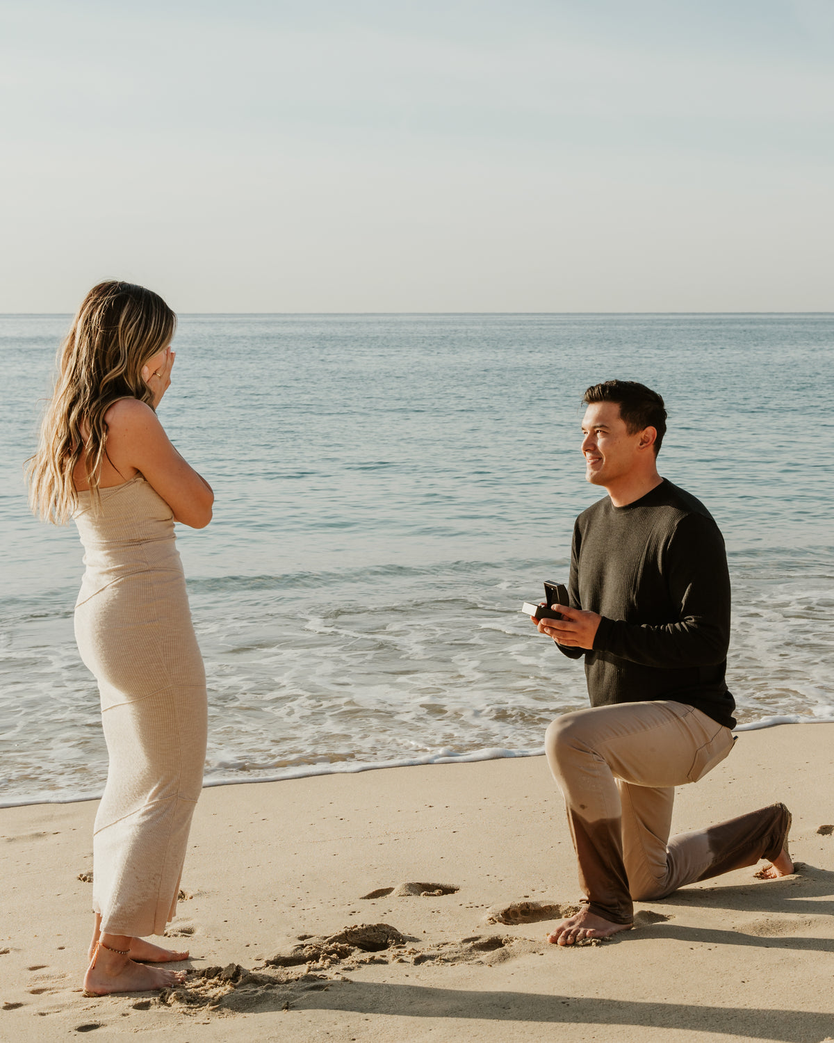 A man kneels on the beach proposing to a woman near the ocean at Marquis Los Cabos