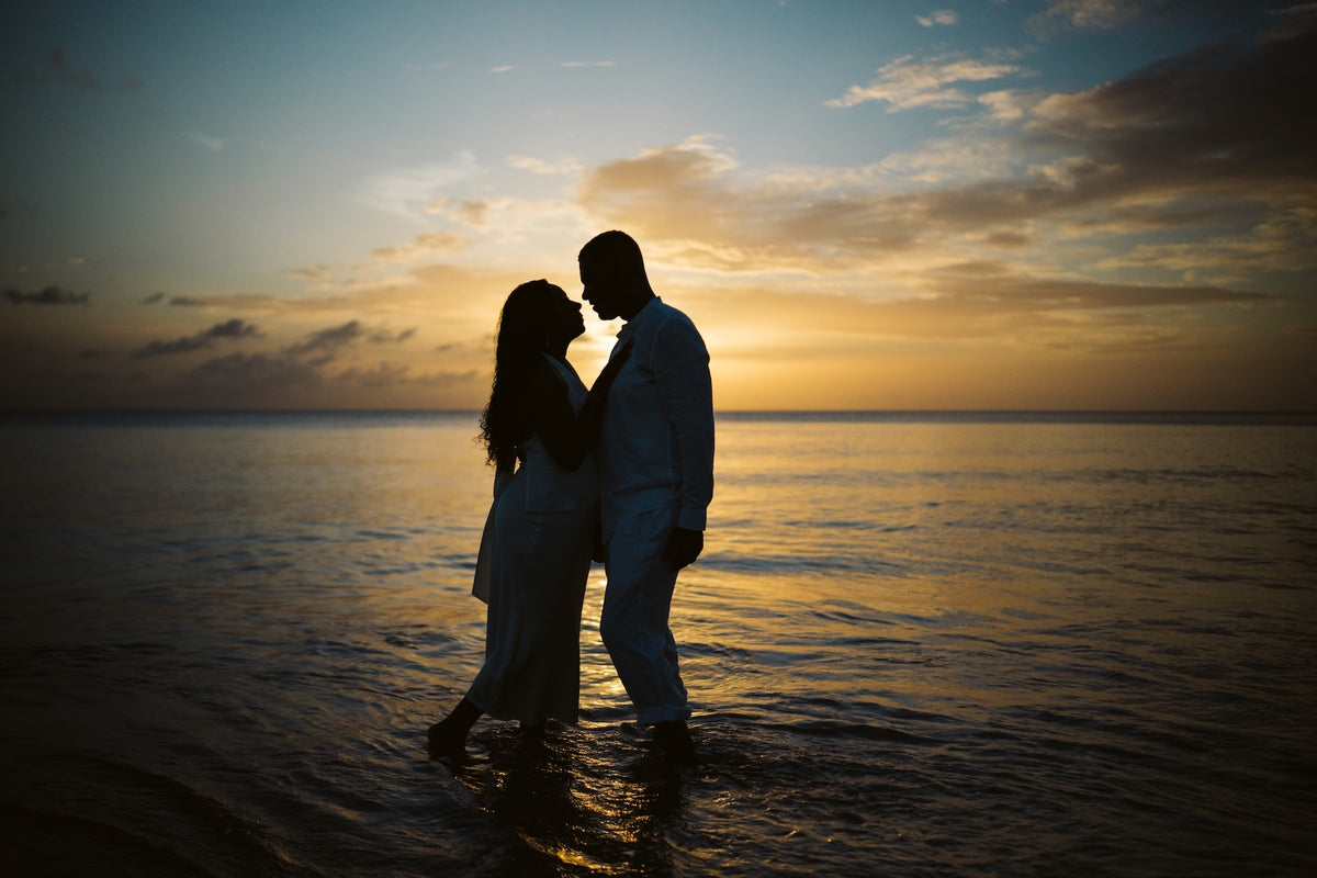 Silhouette of a couple standing in shallow ocean water at sunset, foreheads close together