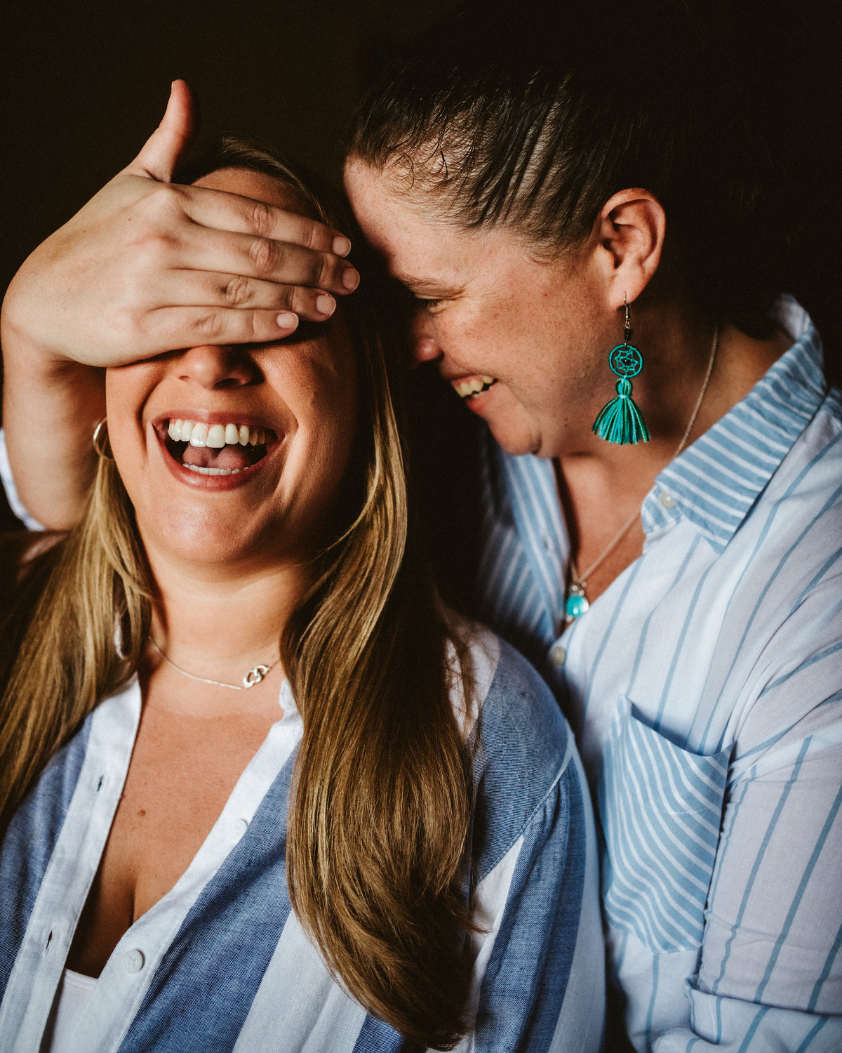 Two women laugh closely together at Valentin Imperial Riviera Maya, one covering the other's eyes with her hand