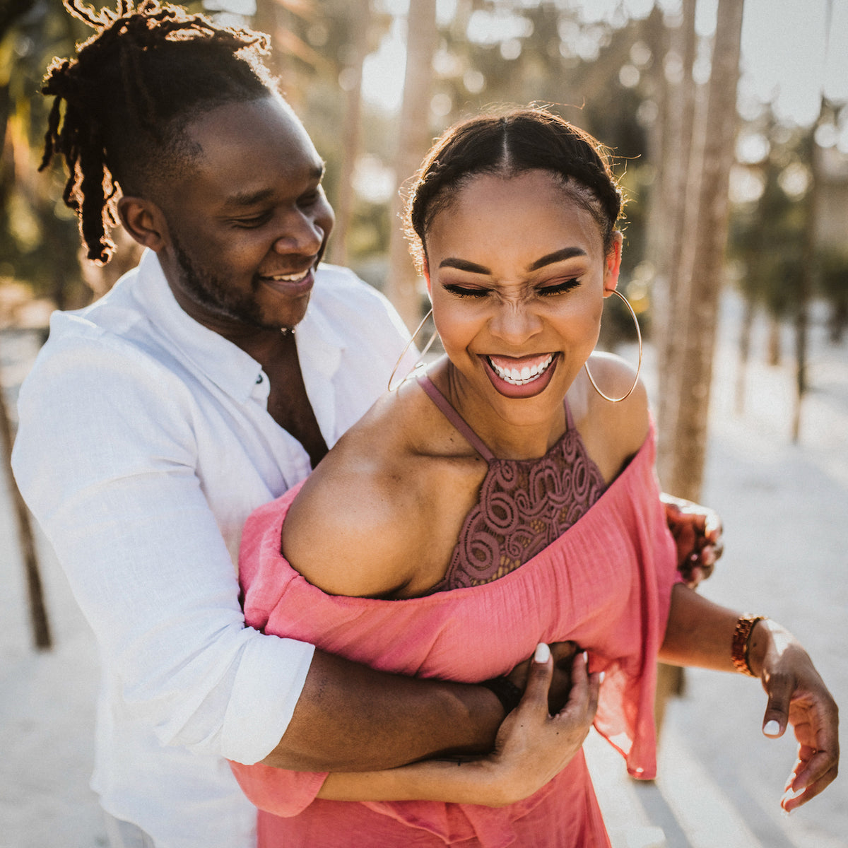 A man embraces a laughing woman from behind on a tree-lined path at Valentin Imperial Riviera Maya