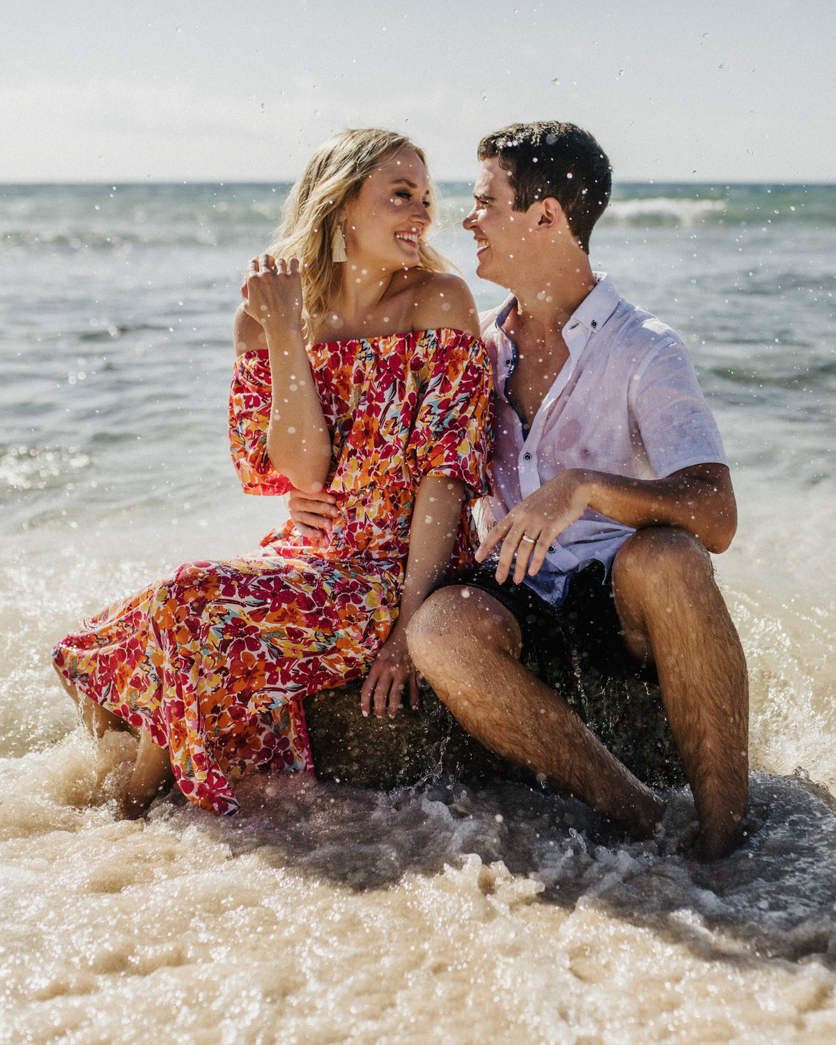 A couple sits together in the surf at Valentin Imperial Riviera Maya, laughing with ocean waves splashing around them