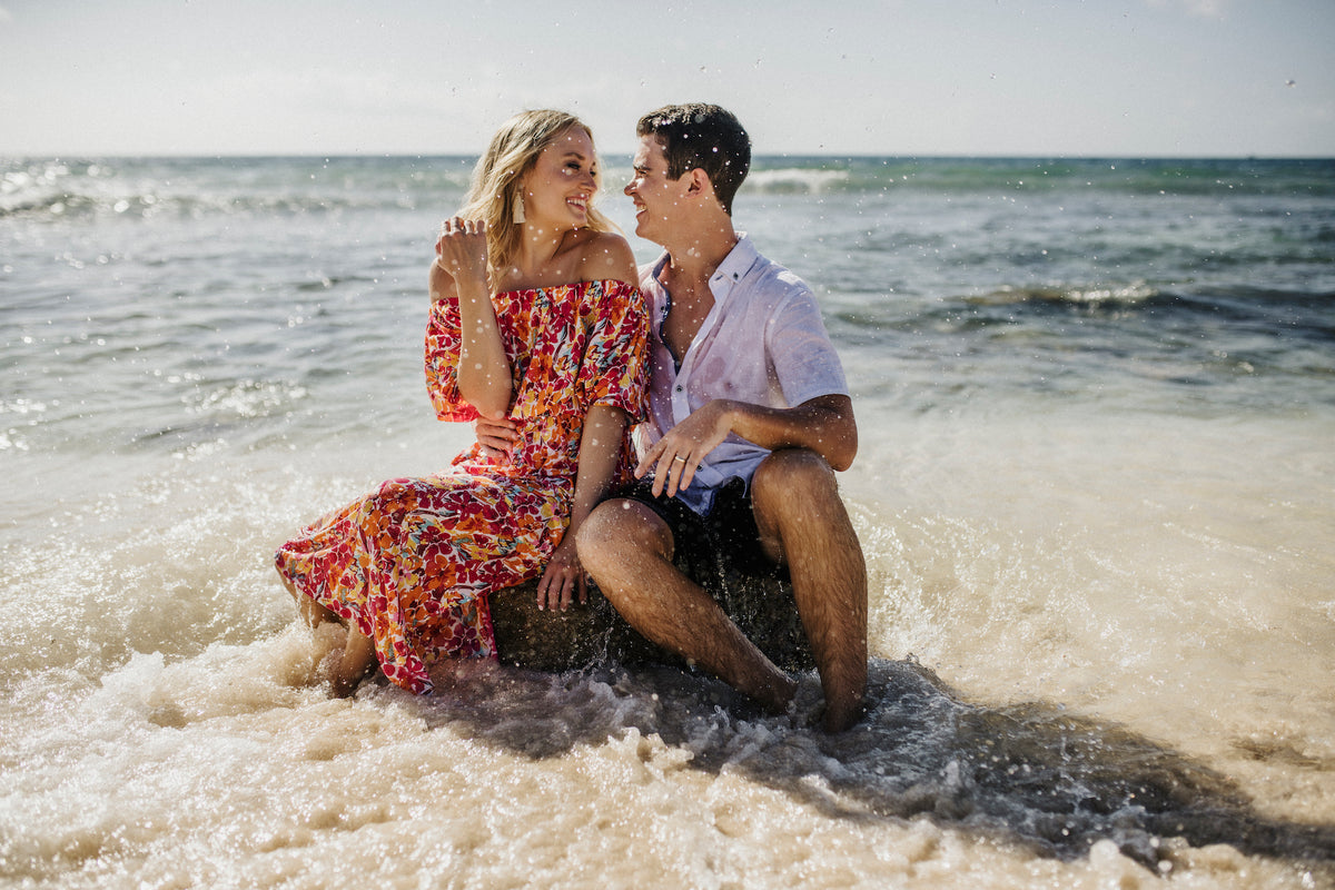 A couple sitting together on rocks in shallow ocean waves at Valentin Imperial Riviera Maya, Mexico