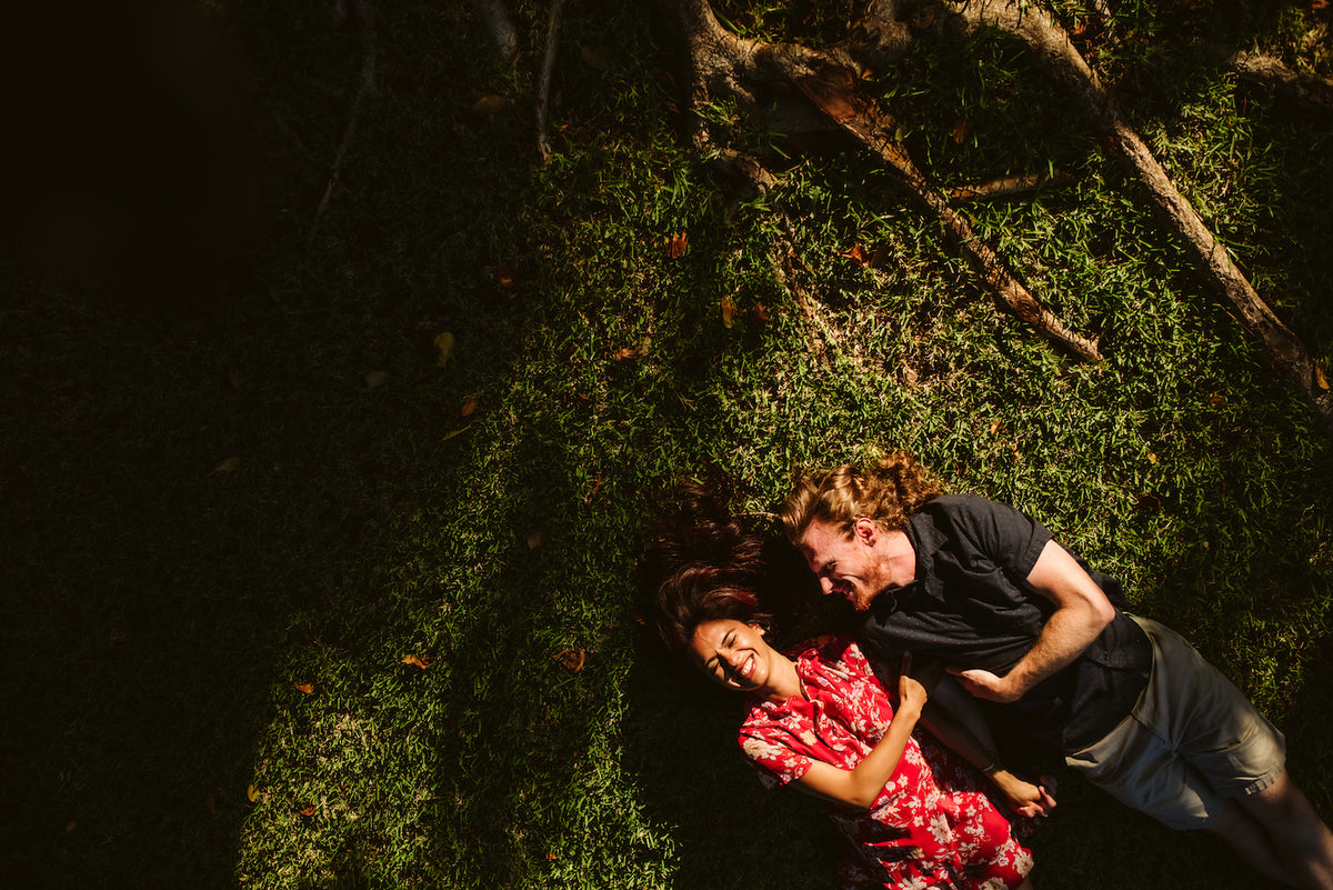 Overhead view of a couple lying on grass beneath tree roots at Valentin Imperial Riviera Maya, Mexico, laughing together