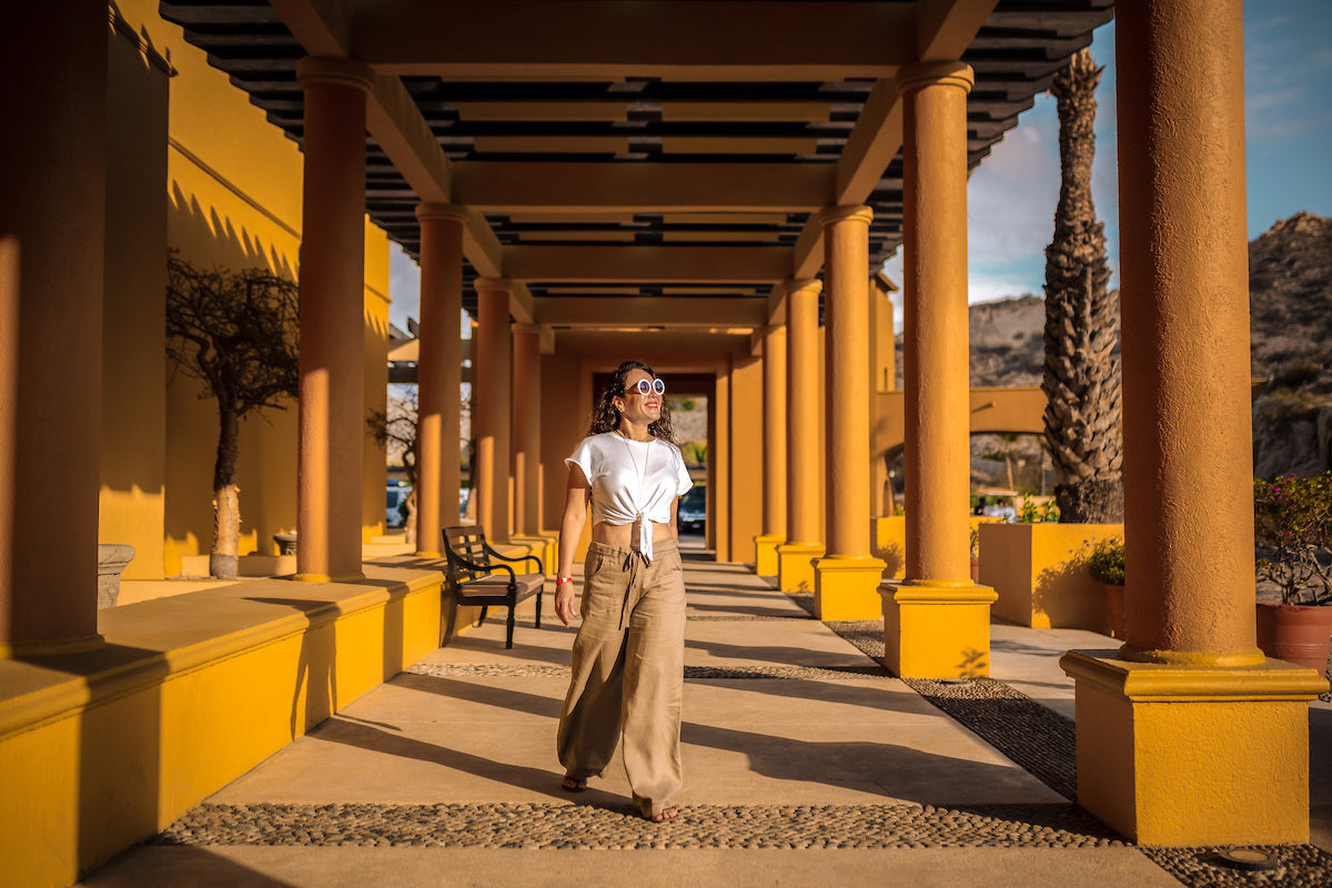 Woman in sunglasses walks through a golden colonnade during a lifestyle photoshoot at Grand Fiesta Americana Los Cabos