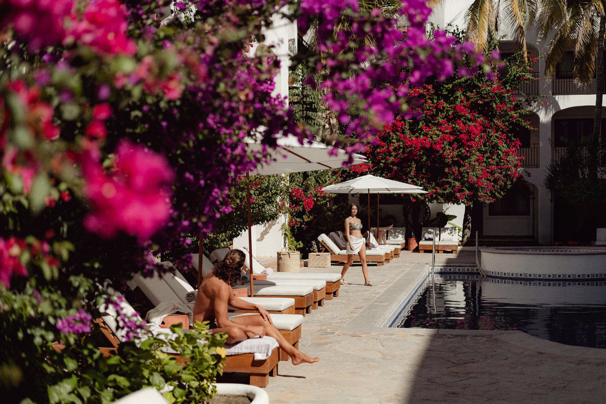 Poolside loungers framed by bougreads at a DreamArt resort, a woman walking as a man sits