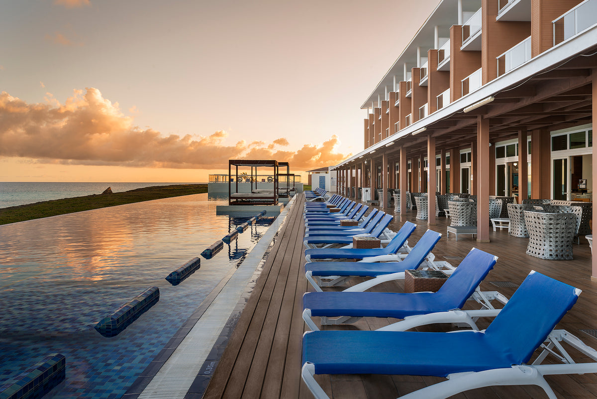 Warm sunset light over blue loungers and an infinity pool next to an oceanfront resort, hotel photography