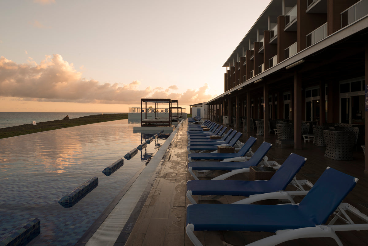 Row of blue sun loungers along an infinity pool at dusk beside a seafront hotel