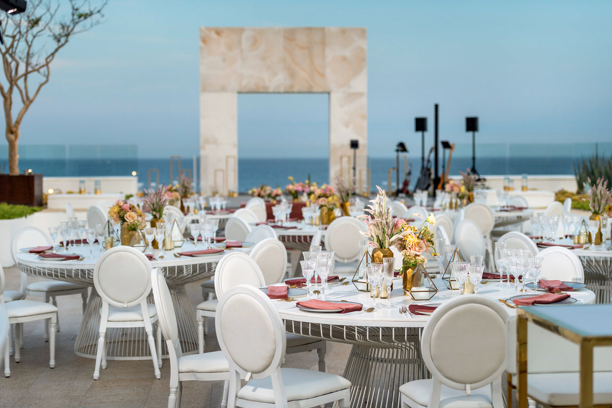 Elegant wedding reception tables with white chairs and floral centerpieces on an oceanfront terrace