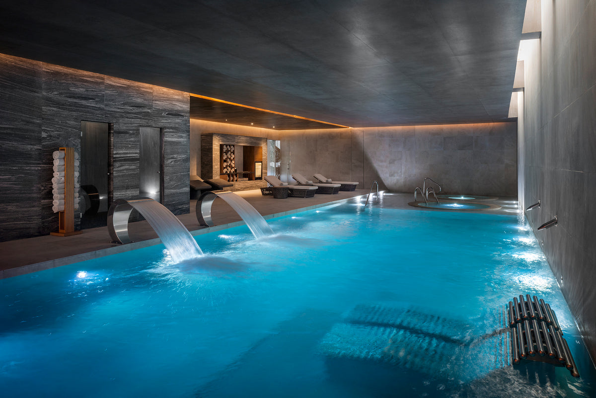 Turquoise indoor thermal pool with cascading water spouts and stone walls in a resort spa