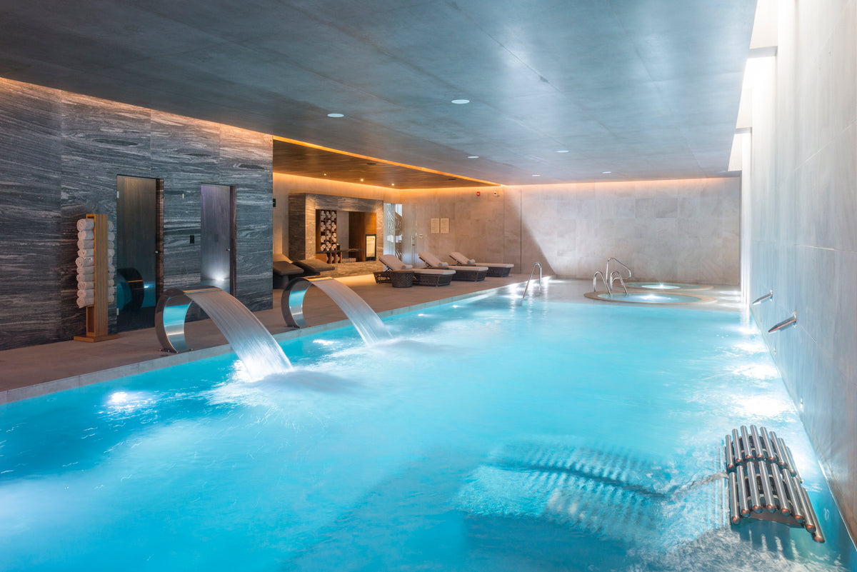 Indoor spa pool with waterfall jets and loungers under warm lighting, hotel spa photography