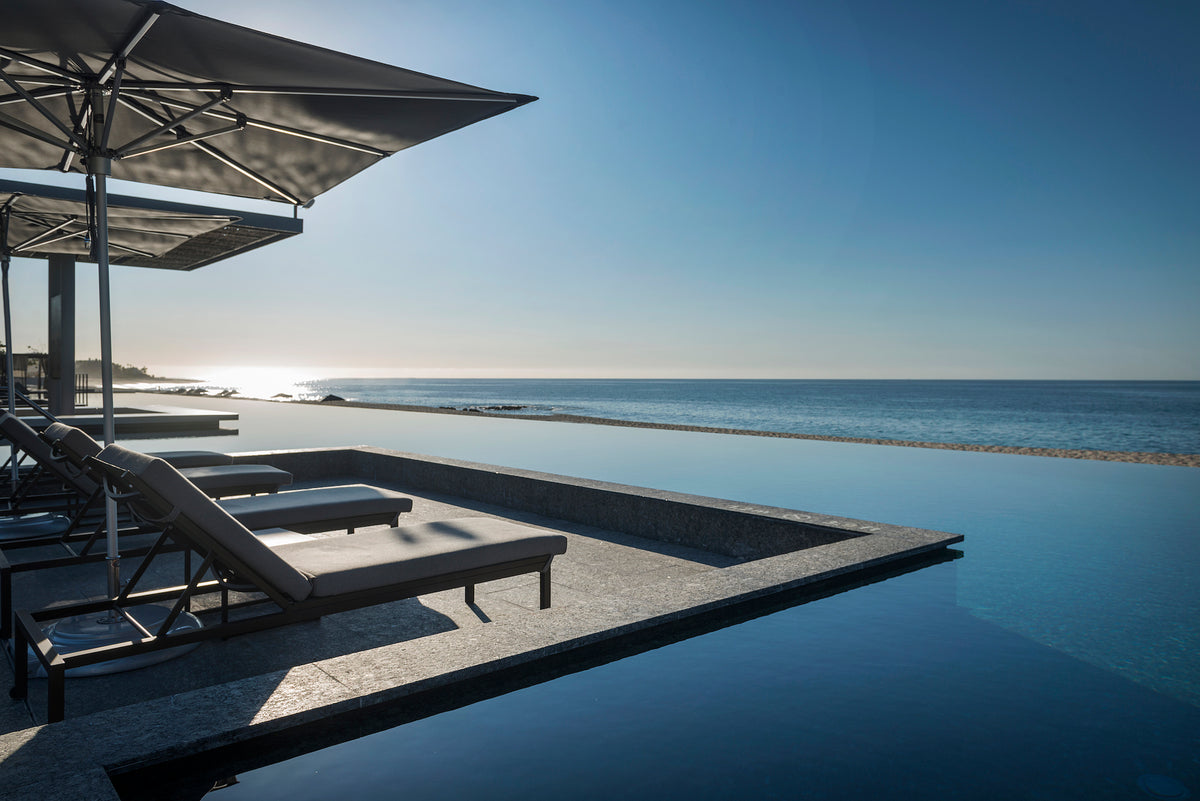 Infinity pool with grey loungers and umbrellas overlooking the ocean at sunrise, luxury hotel photography