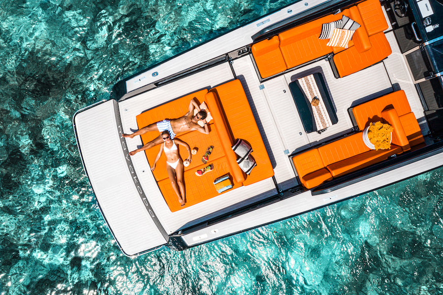 Drone view of a couple sunbathing on orange cushions aboard a yacht over turquoise water