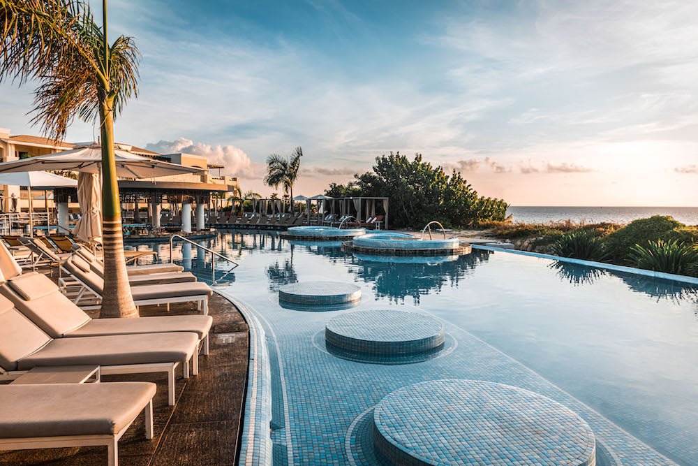 Sunrise over a resort infinity pool with round tiled loungers, palm trees and the sea beyond