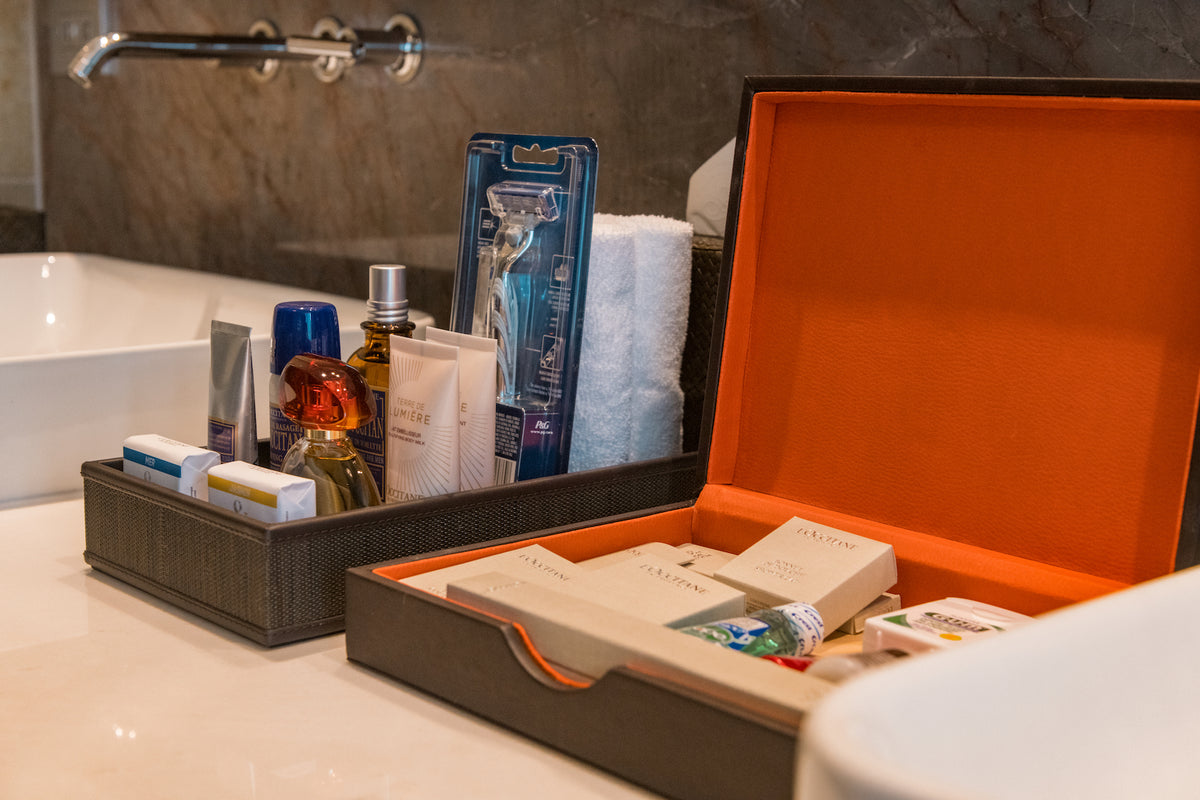 Bathroom amenities with toiletries, razor and an orange-lined vanity box beside a marble sink, hotel amenities photography