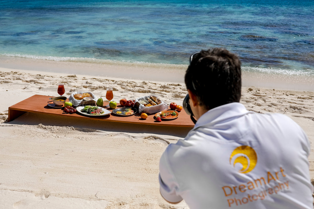 DreamArt photographer shoots a breakfast spread on a wooden board set on the beach by the sea