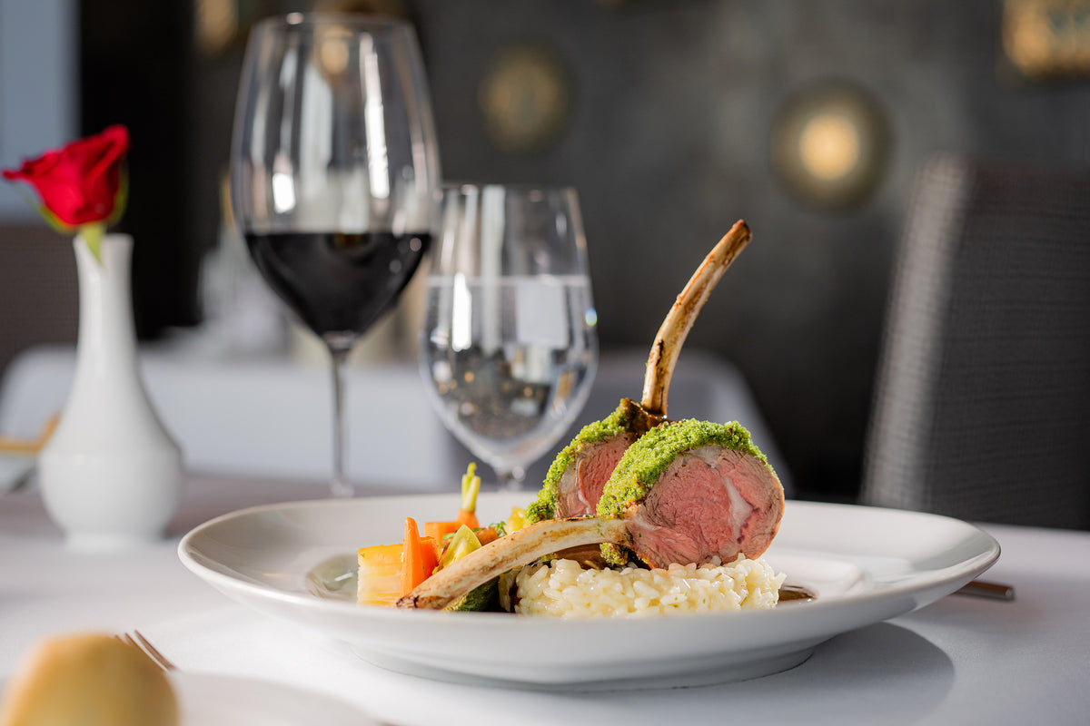 Herb-crusted rack of lamb on risotto with red wine and a rose, food photography at Marquis Los Cabos