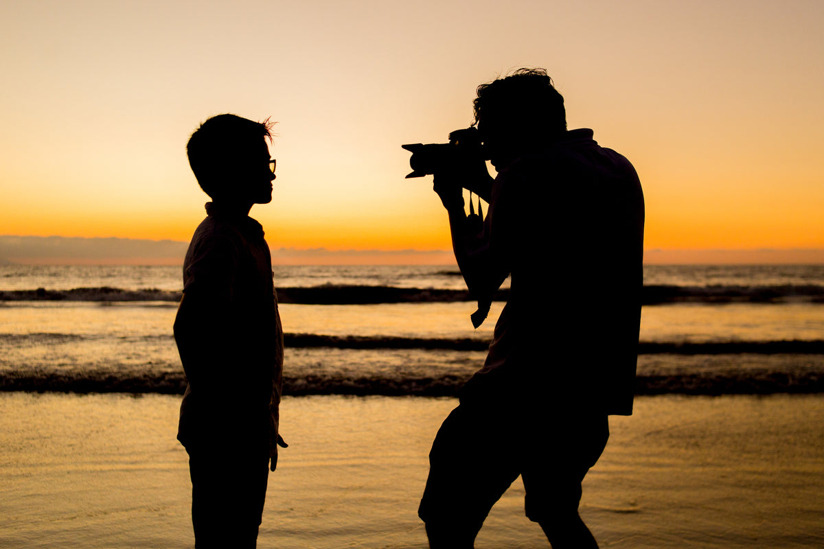 Silhouette of a photographer shooting a young boy on the beach at sunset in Mexico