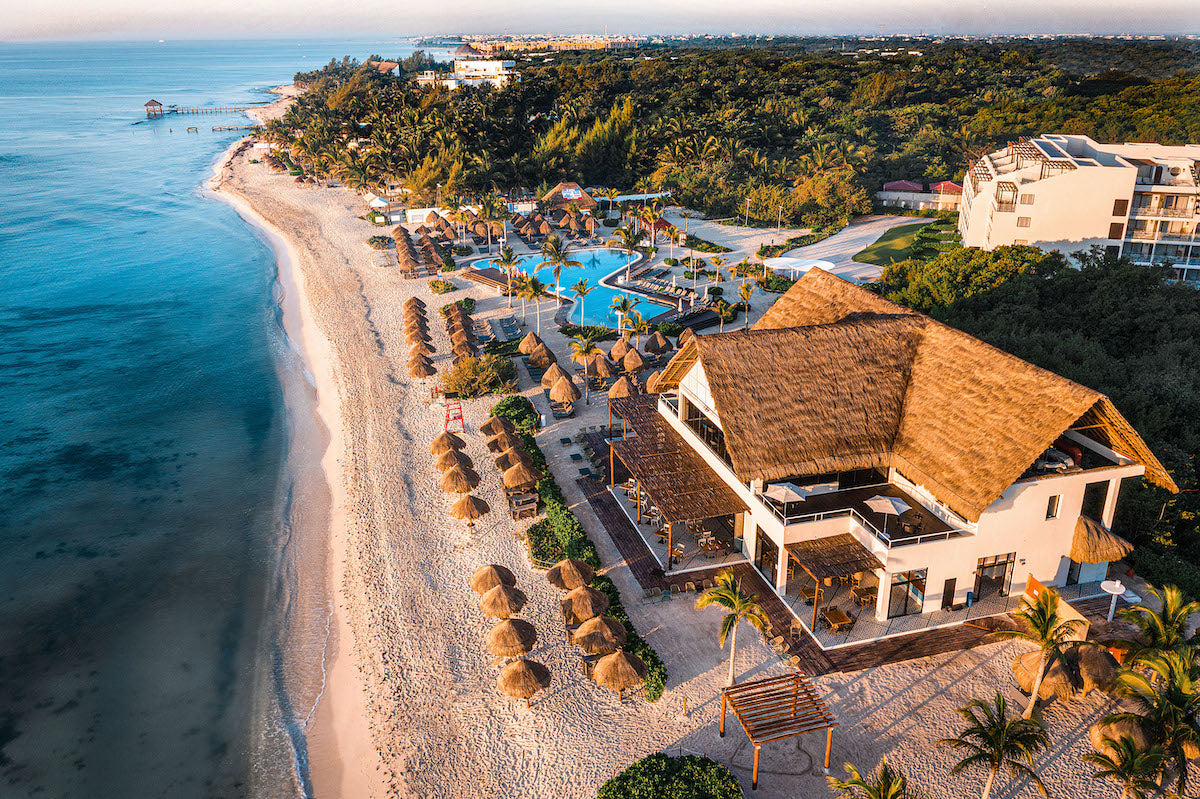 Drone view of the beach club, palapa umbrellas and pools along the shore at Ocean Riviera Paradise