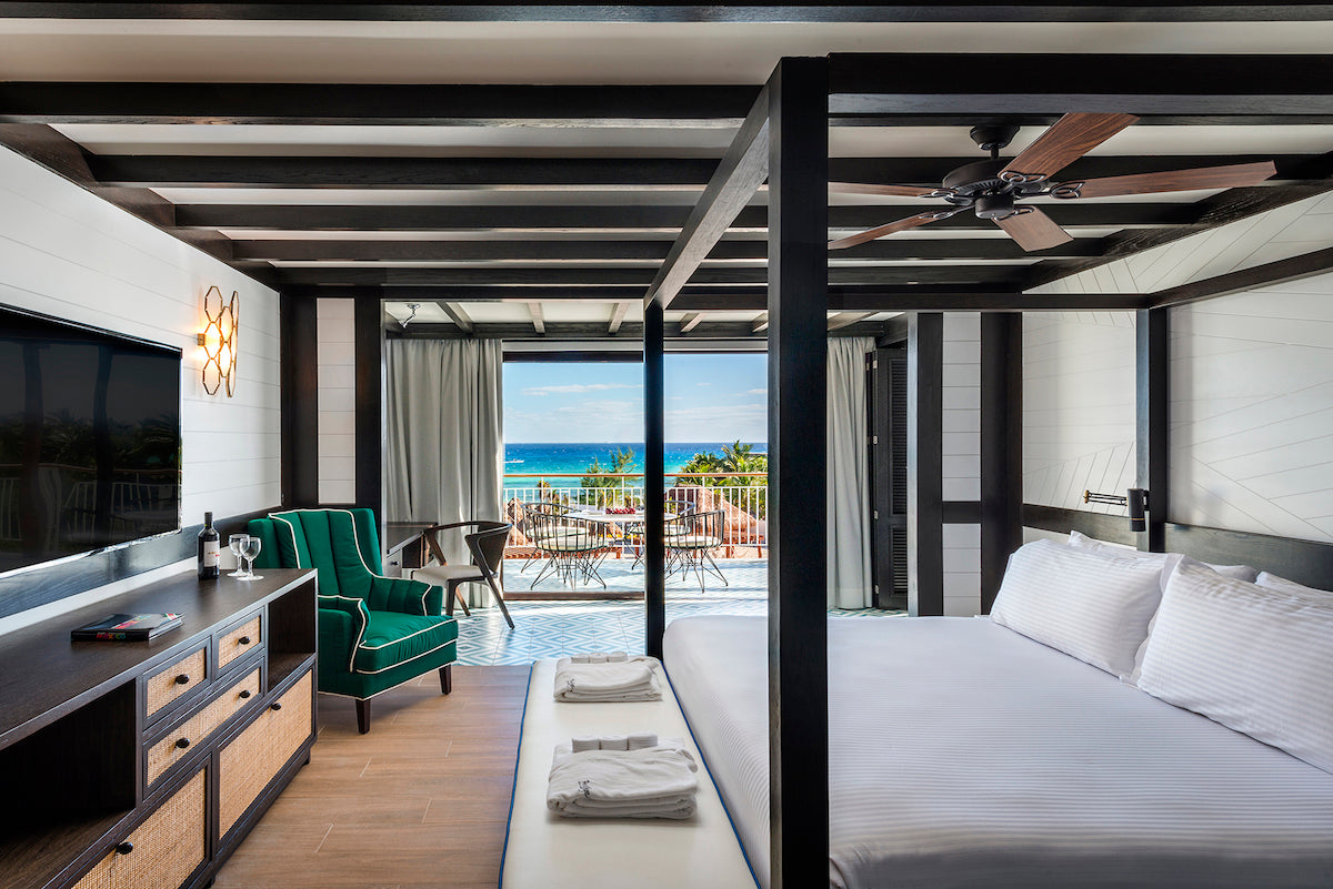 Hotel room with a four-poster bed and green armchair opening onto an ocean-view terrace at Ocean Riviera Paradise