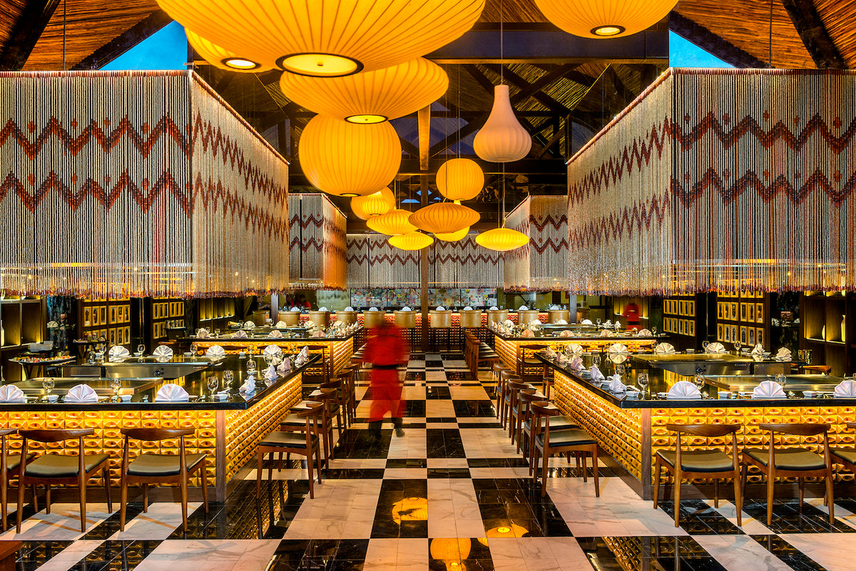 Warm-lit restaurant with glowing lanterns and a server in red crossing the checkered floor at Ocean Riviera Paradise