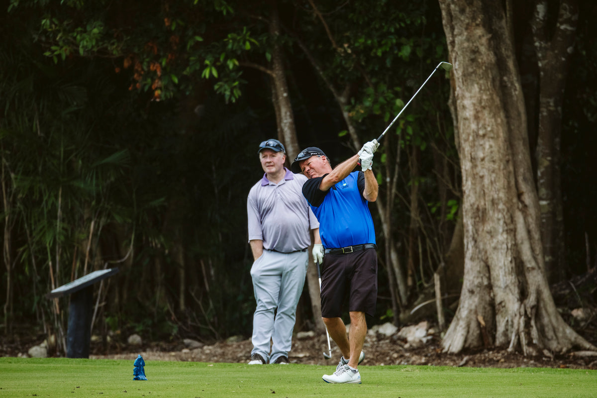 Golfer tees off on a jungle-lined course during a corporate golf tournament event