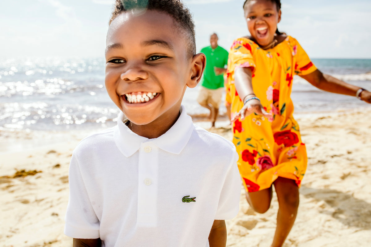 Smiling boy in a white polo races his sister along the beach as dad follows at Playacar Palace
