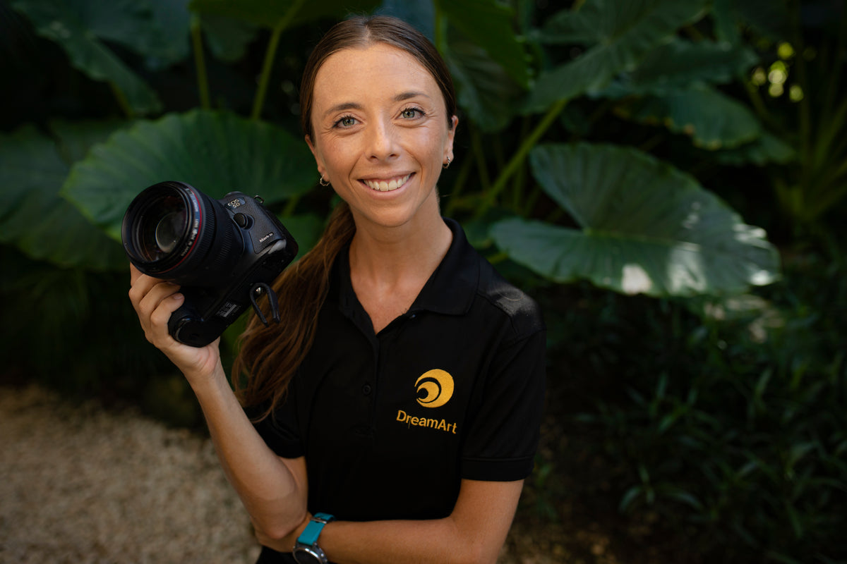 Smiling female DreamArt event photographer holding her camera in front of tropical foliage