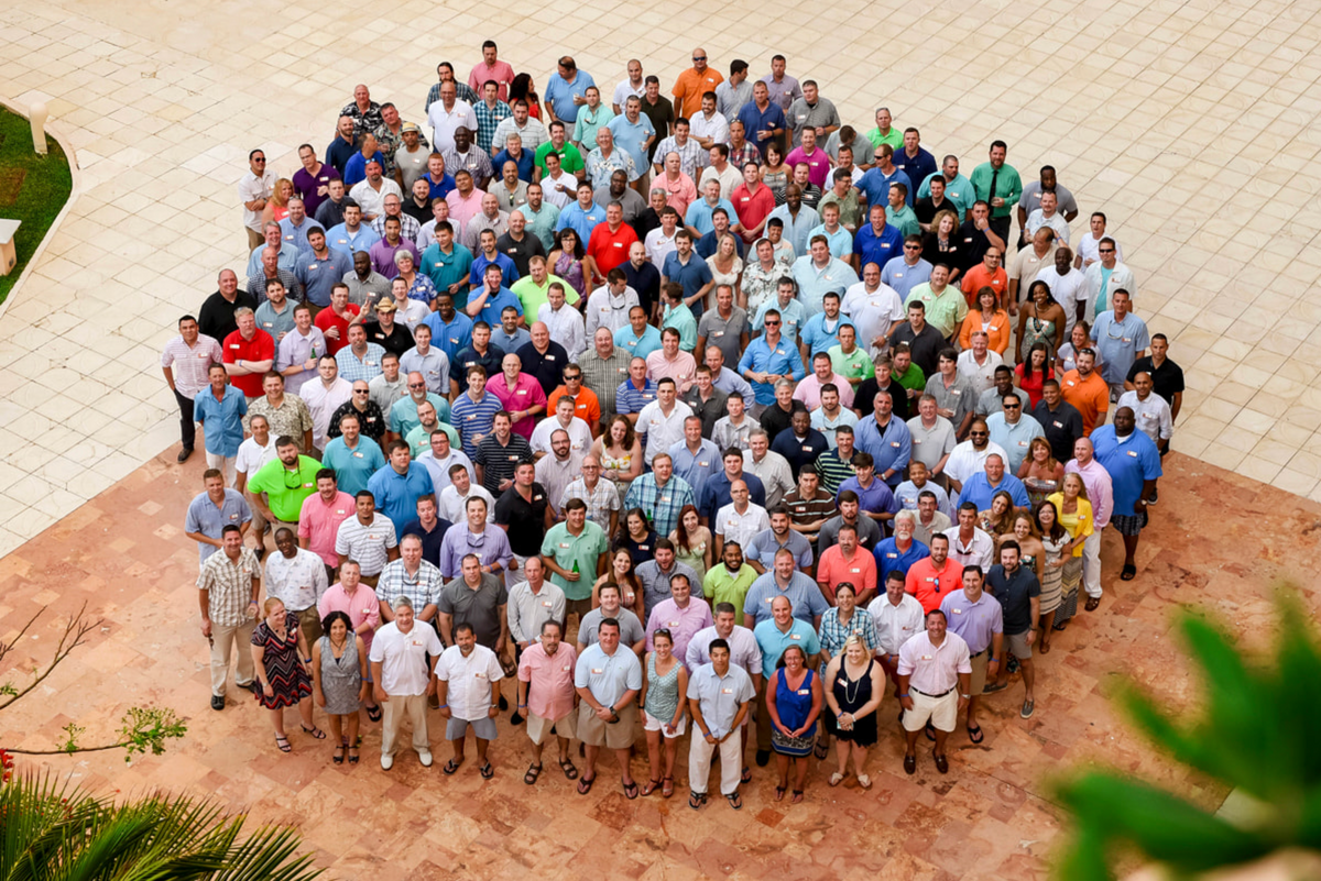 Aerial group photo of a large corporate team gathered on a resort plaza