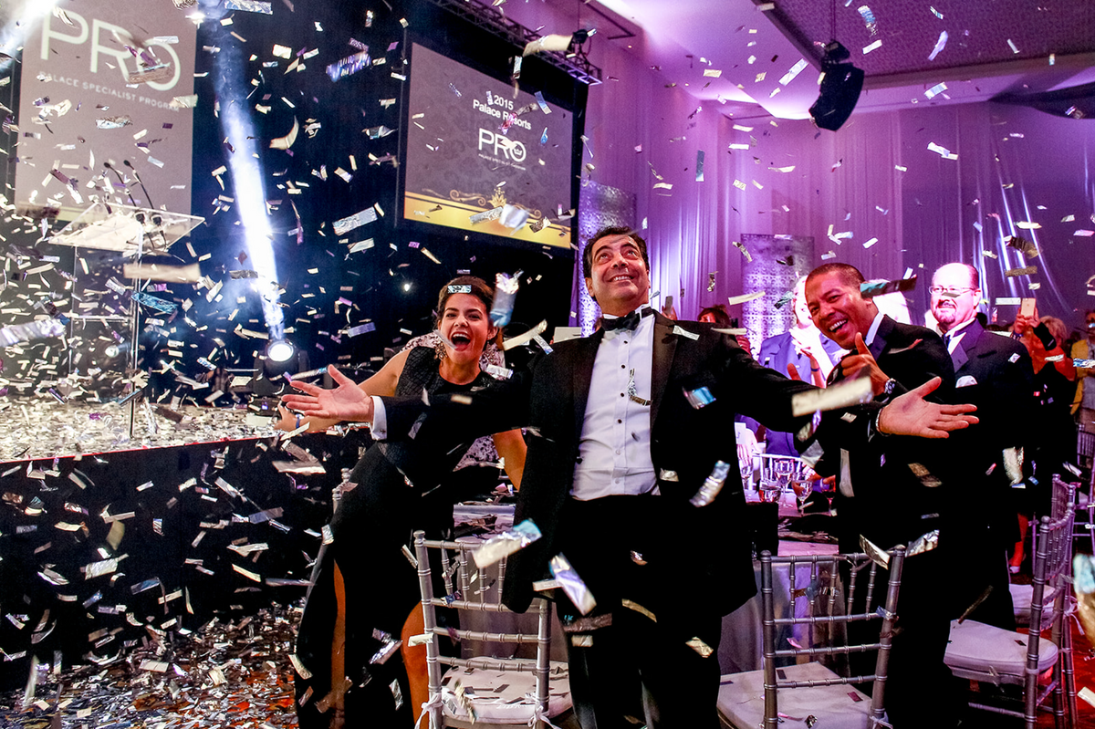 Executives celebrate under falling confetti and spotlights at a corporate launch party