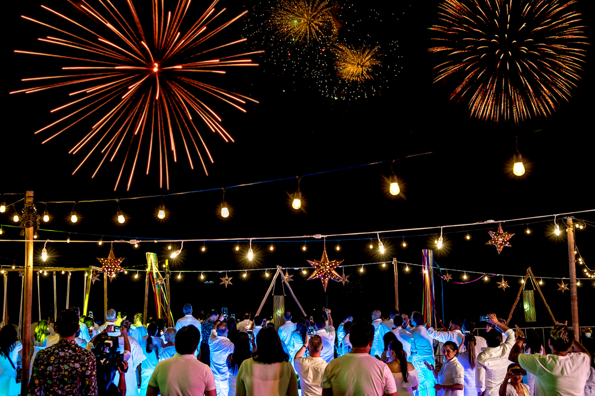 Fireworks burst over guests dressed in white at a festive outdoor private celebration