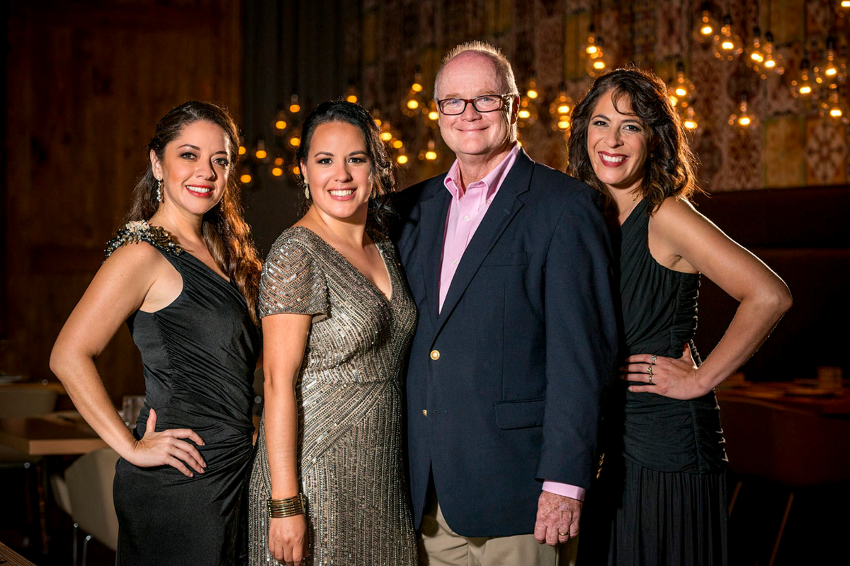 Four guests in evening wear pose together in a warmly lit restaurant during a private event