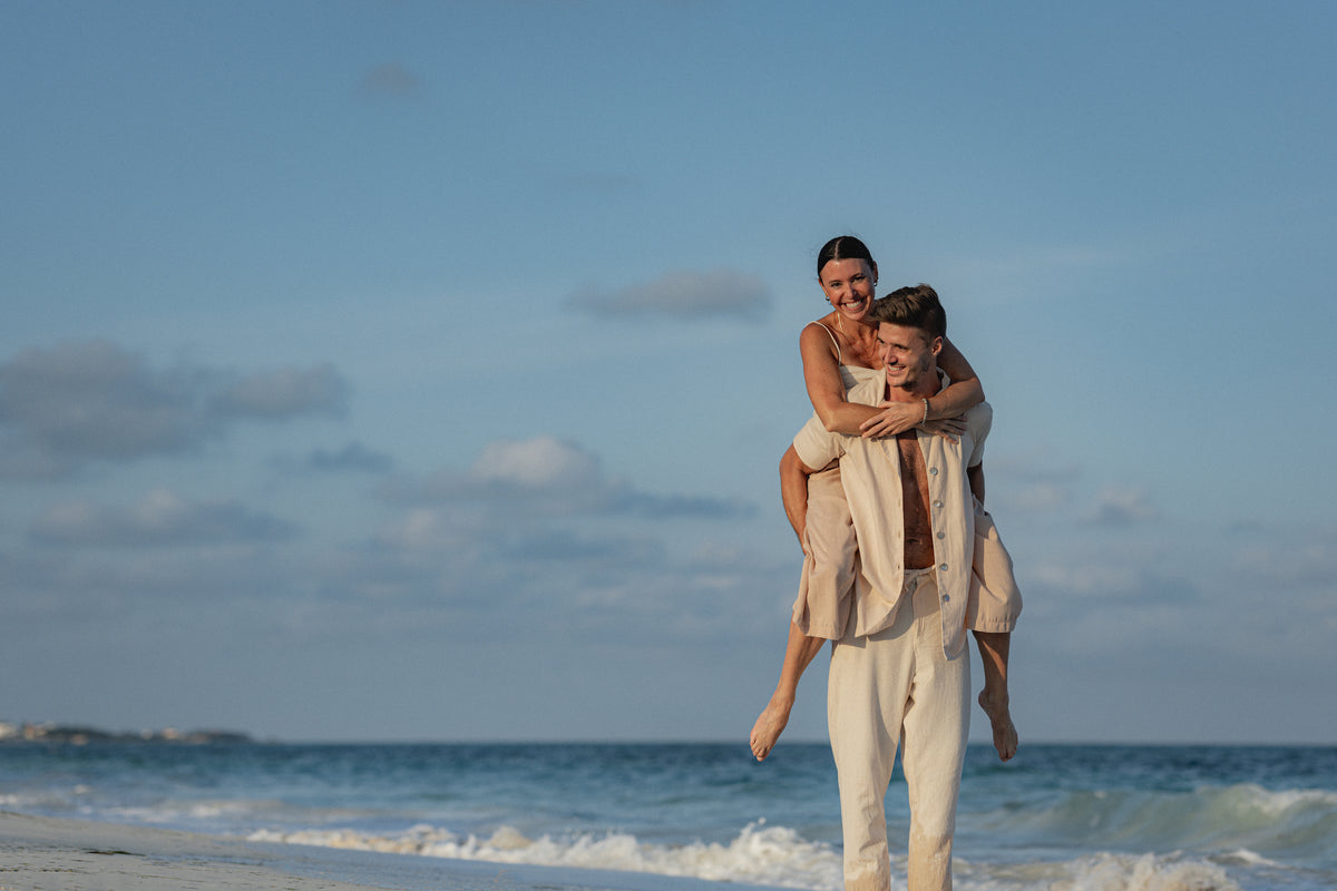 Man gives his laughing partner a piggyback ride along the shoreline at Secrets Playa Blanca Costa Mujeres