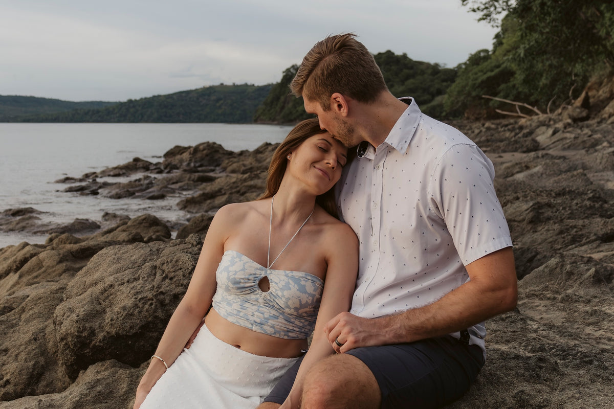 Man kisses his partner's forehead as they sit on the rocks by the bay at Secrets Papagayo Costa Rica