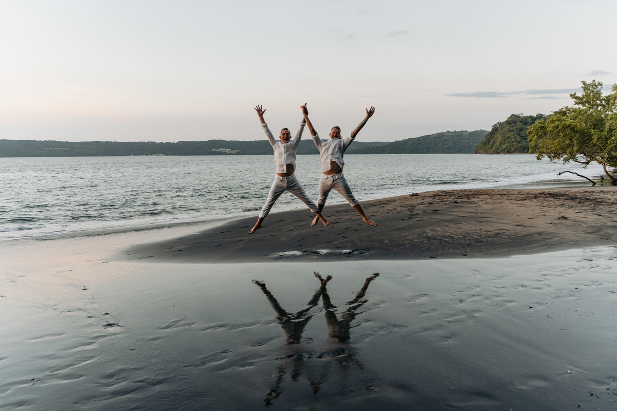 Two men leap in matching star jumps, reflected on the wet sand at Secrets Papagayo Costa Rica