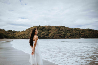 Image of woman standing on the beach in a white dress, posing for a DreamArt photographer, used for blog about Summer Trends 2025  