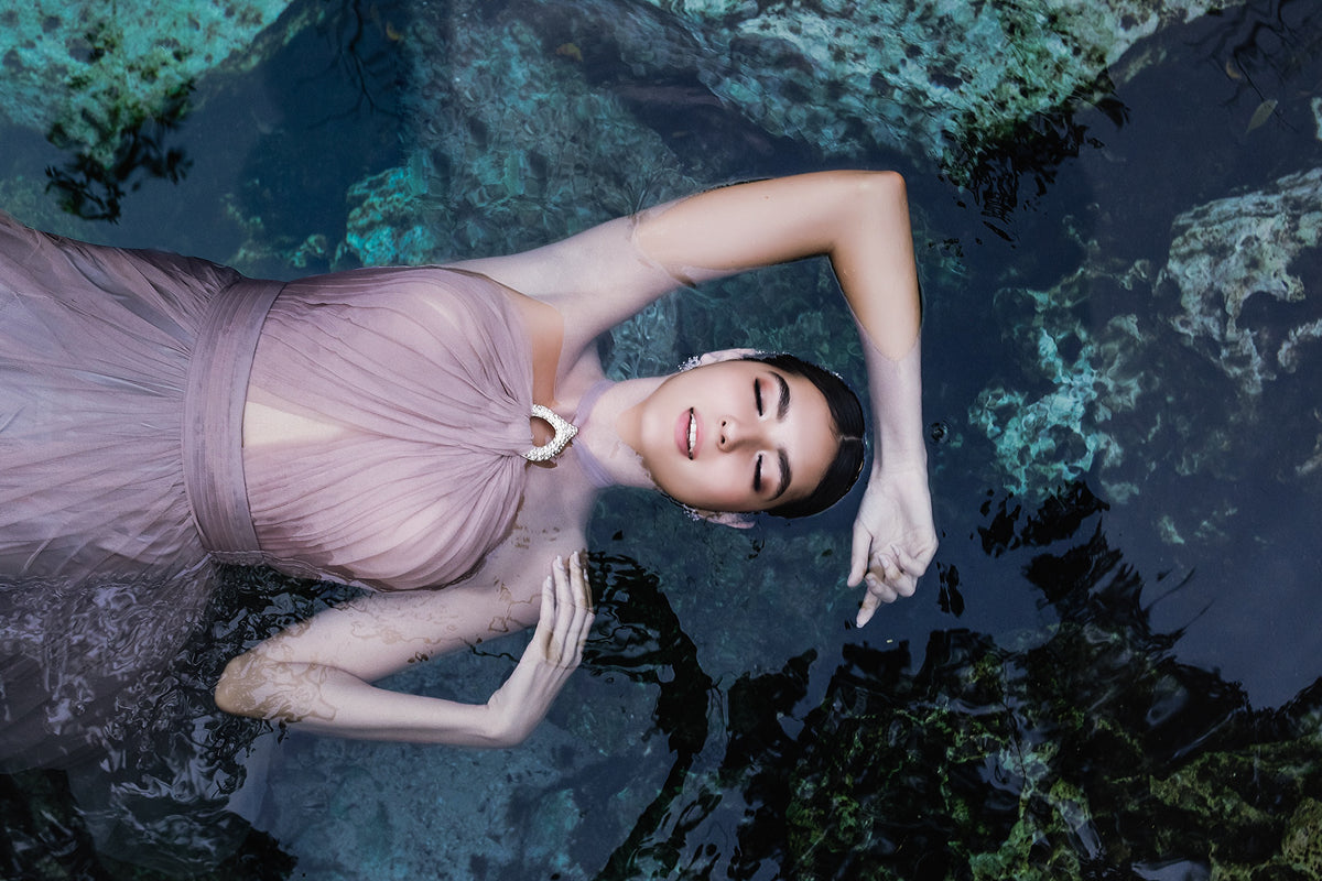 Woman in a blush gown floats on her back in clear cenote water during a trash the dress photoshoot