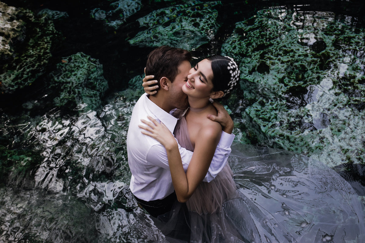 Groom kisses the bride's cheek as they stand waist-deep in a cenote during their trash the dress photoshoot