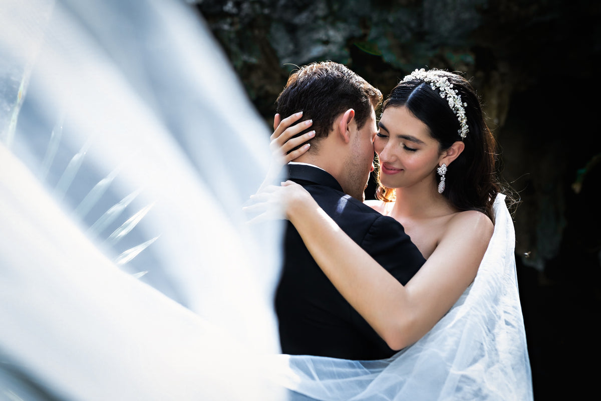 Bride's veil billows across the frame as she embraces the groom in a shaded cenote
